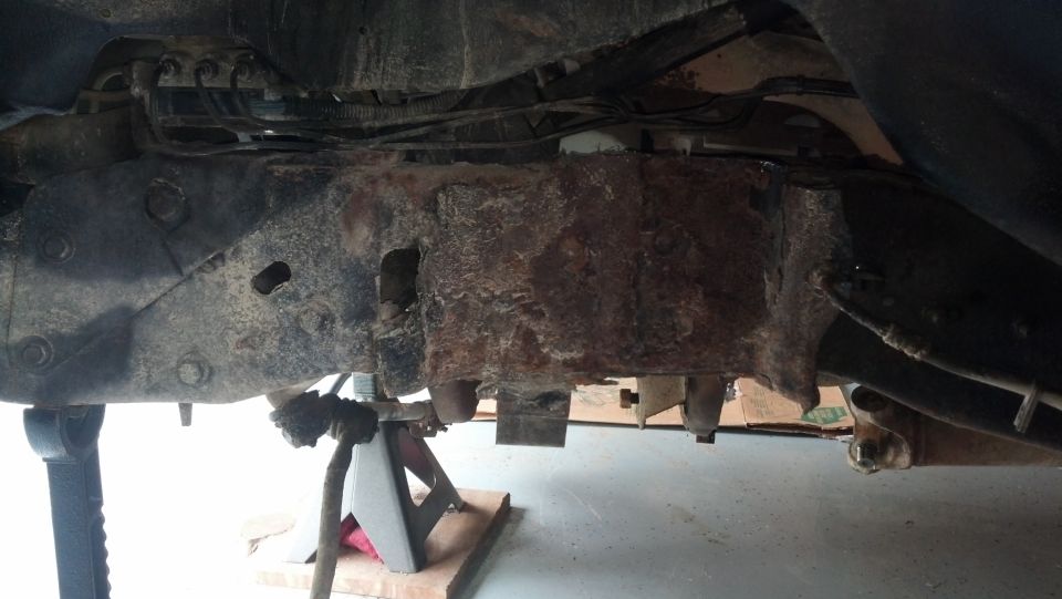 Heavily rusted vehicle frame and suspension components supported by jack stands.
