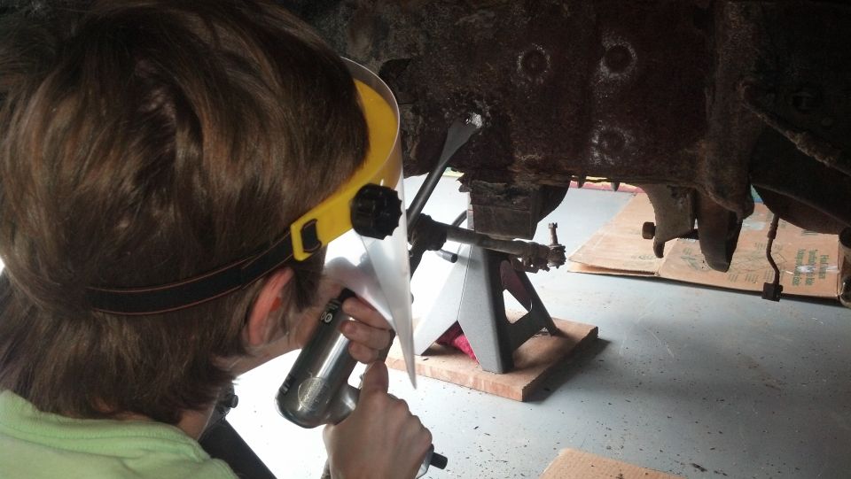 Person working on rusty vehicle undercarriage with tool.