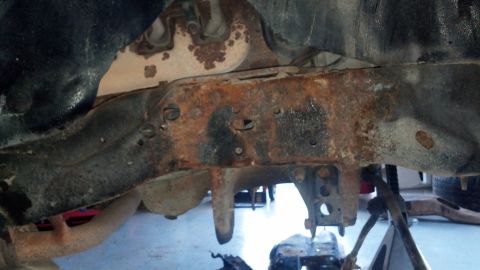 1996 Ford Bronco - The underside of a vehicle frame shows significant rust damage and corrosion. Several metal brackets and suspension components are visible,…