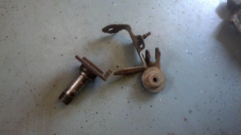 1996 Ford Bronco - Two rusty metal automotive parts are laid out on a speckled gray concrete floor. One part is a cylindrical metal piece with a flange, and t…