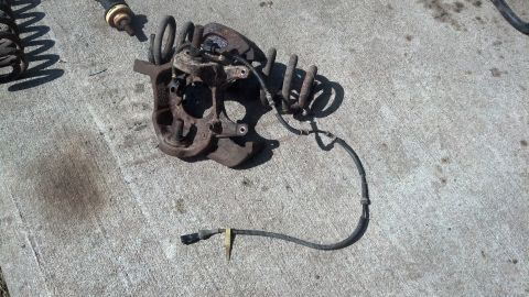 1996 Ford Bronco - A rusty front suspension knuckle assembly with a coil spring and an ABS sensor wire is laid out on a concrete surface. A separate coil spri…