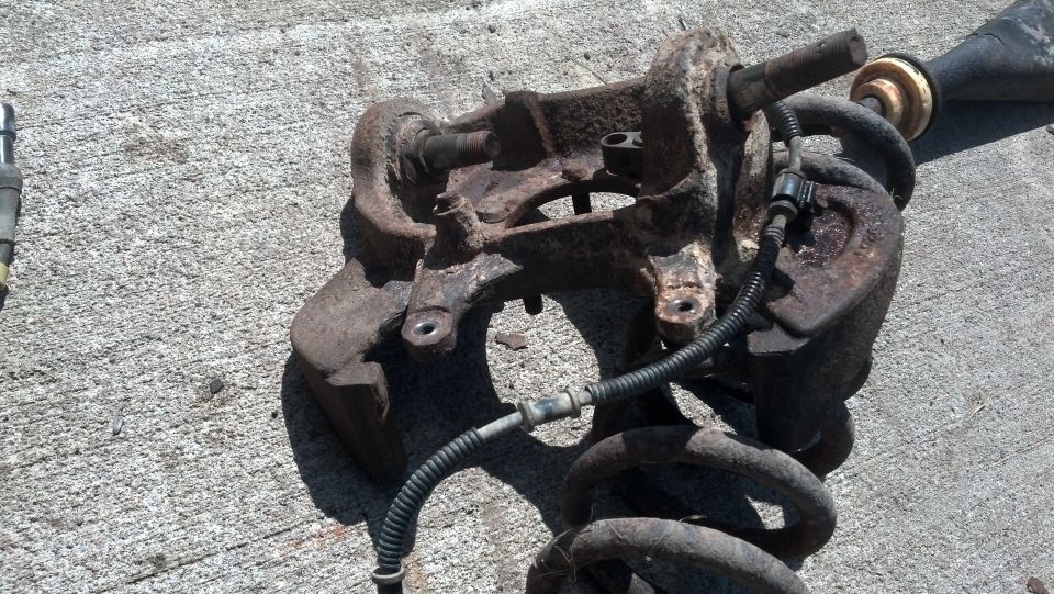 Rusted front suspension assembly with coil spring and spindle on concrete.