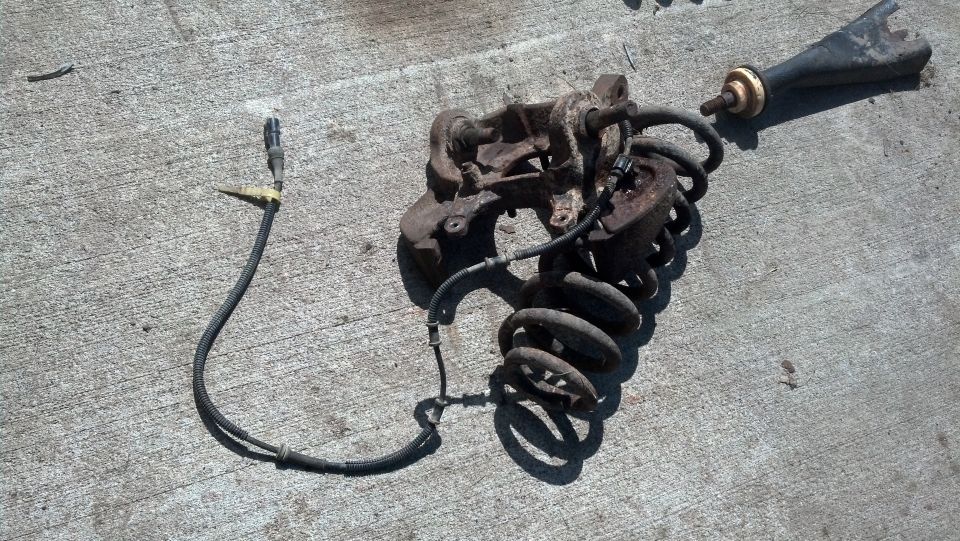 Rusty Ford Bronco suspension assembly with coil spring and shock absorber on concrete.