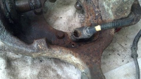 1996 Ford Bronco - A heavily rusted and dirty automotive suspension component, likely a steering knuckle, with a black ABS sensor wire attached. The part is r…