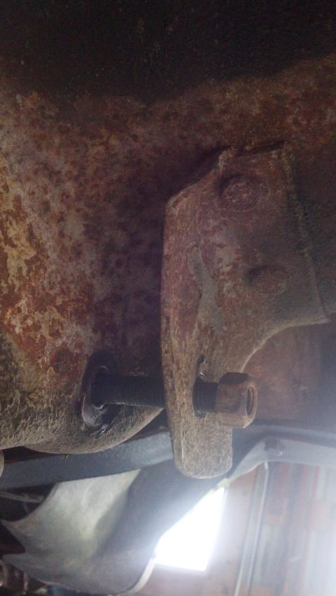 1996 Ford Bronco - A close-up view of a heavily rusted metal bracket with a bolt and nut attached, likely part of a vehicle's undercarriage.