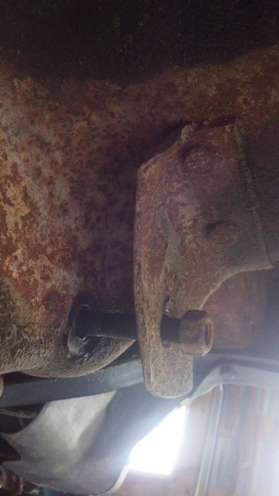 Close-up of rusted metal bracket with bolt and nut on a vehicle's undercarriage.