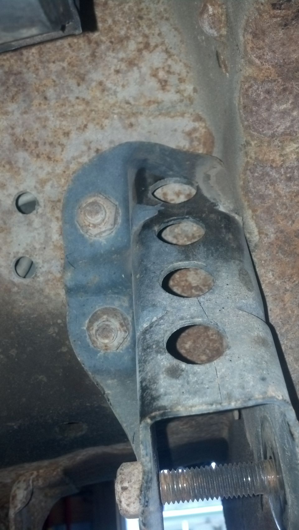 Close-up of rusty metal brackets and bolts on a vehicle's undercarriage.