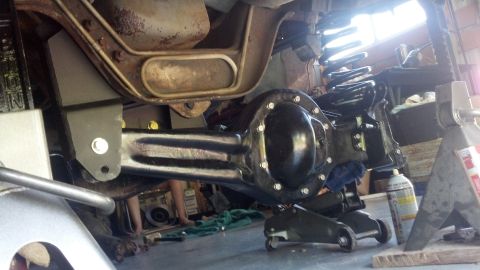 1996 Ford Bronco - A black rear differential assembly is supported by jack stands and a floor jack underneath a vehicle. The vehicle's suspension components,…