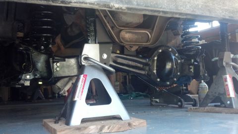 1996 Ford Bronco - The underside of a vehicle, likely a Ford Bronco, is supported by jack stands with the suspension components visible. The rear axle assembl…