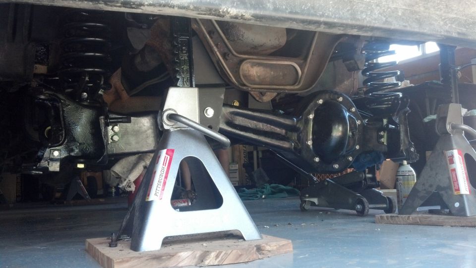 Underside of a vehicle on jack stands, showing rear axle and suspension.