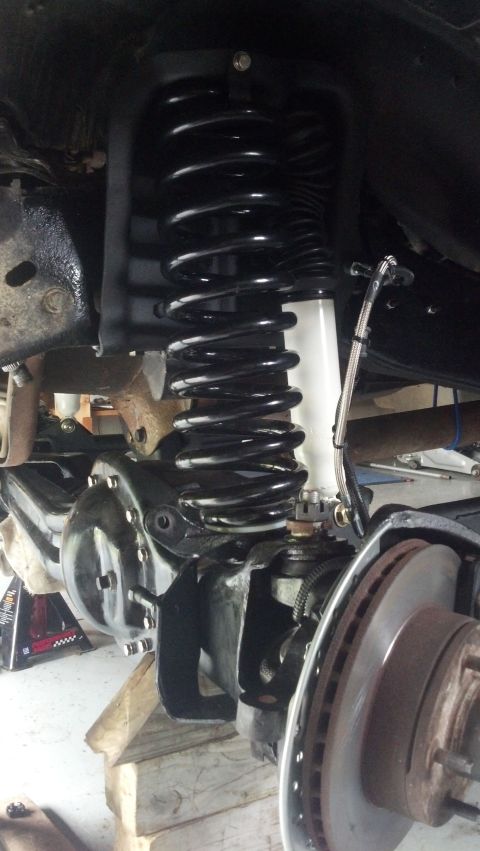 1996 Ford Bronco - A close-up, low-angle view of the front suspension of a 1996 Ford Bronco, showing a new black coil spring and white shock absorber installe…