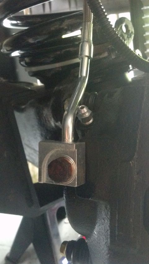 1996 Ford Bronco - A close-up view shows a metal brake line assembly connected to a square metal bracket, which is mounted to a black suspension component. A…