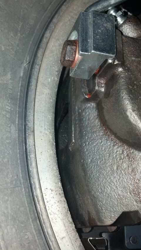 1996 Ford Bronco - A close-up view of a brake caliper assembly with a copper washer visible on a bolt, positioned next to a tire and wheel rim.
