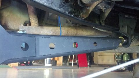 1996 Ford Bronco - The underside of a vehicle shows a black, rectangular control arm with circular cutouts, attached to a bracket with a yellow bushing. A rus…