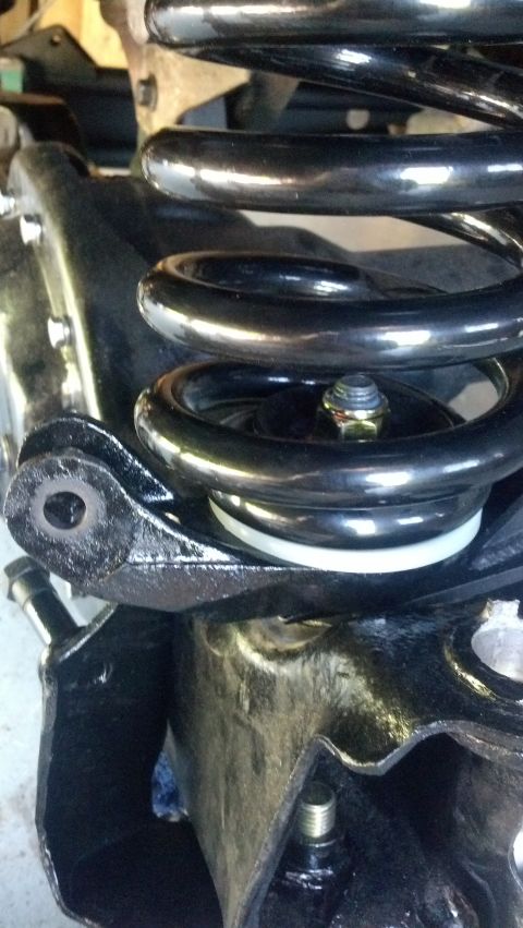 1996 Ford Bronco - A close-up view shows the suspension system of a vehicle, featuring a black coil spring mounted on a black bracket with a white spacer and…