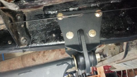 1996 Ford Bronco - A black metal bracket is bolted to the underside of a vehicle frame, with a cable running through it. A suspension component with rubber bu…
