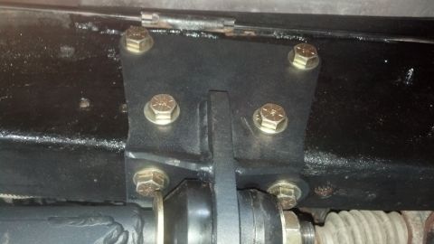 1996 Ford Bronco - A black metal bracket is bolted to the frame of a vehicle with six gold-colored bolts. A black rubber component is attached to the bracket…