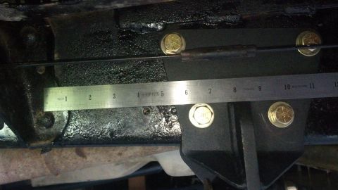 1996 Ford Bronco - A metal ruler is placed against a black metal bracket bolted to a vehicle's frame. The ruler shows measurements in inches, with the bracket…