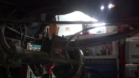 1996 Ford Bronco - The underside of a vehicle, likely a 1996 Ford Bronco, shows the rear axle assembly with leaf springs and brake components. The scene appea…
