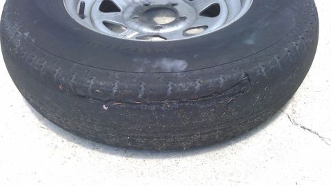 1994 Ford Bronco - A close-up view of a damaged tire on a vehicle, showing significant wear and a large gash on the sidewall. The tire is mounted on a silver…