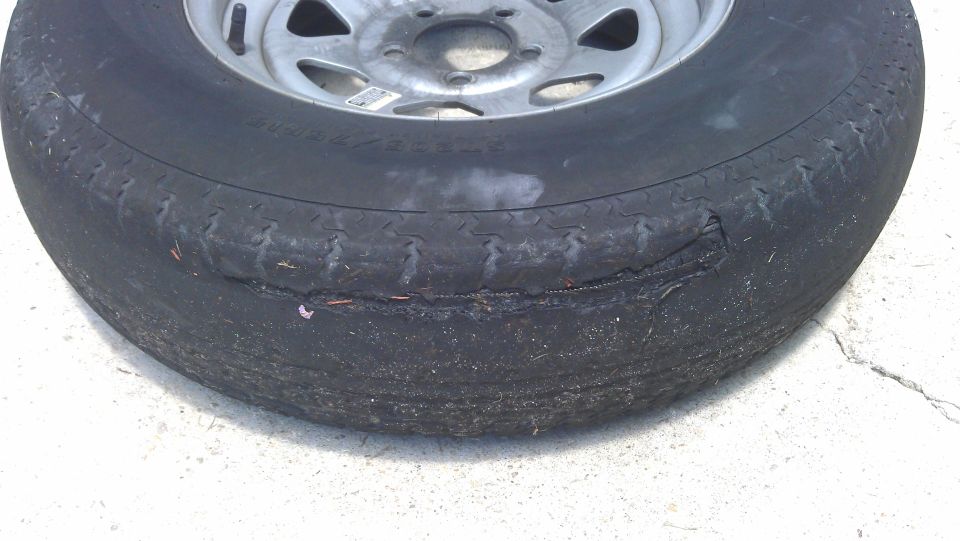 Damaged tire with a gash on the sidewall, mounted on a silver rim.