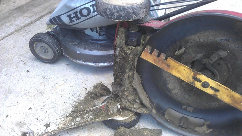 Red Honda lawnmower tipped on side, showing blade and grass clippings.