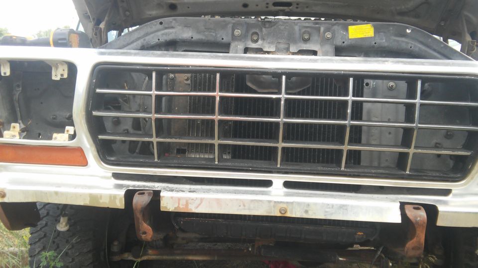 Front view of a classic Ford truck grille and bumper, hood open.