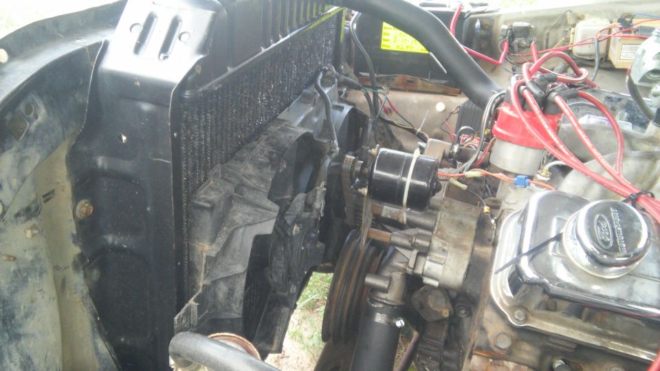 Engine bay with radiator, fan shroud, chrome Ford valve cover, red plug wires and belts