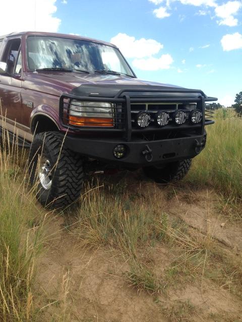 1996 Ford Bronco - Low front three-quarter view of a burgundy Ford Bronco with a black steel winch bumper, full grille guard and light bar carrying four round…