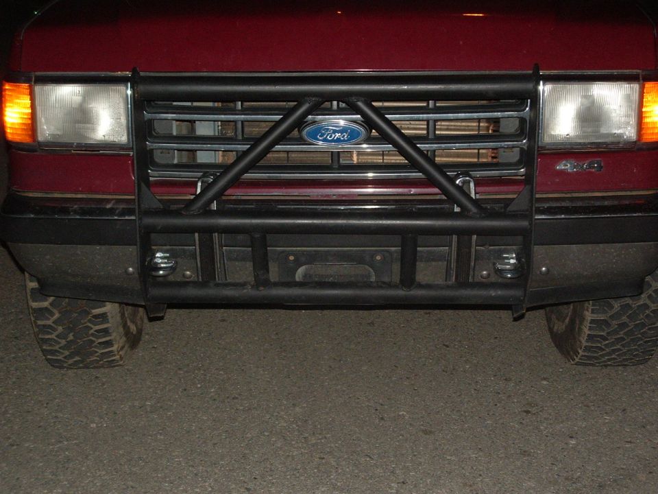 Black tubular brush guard with Ford oval over the grille of a maroon truck at night