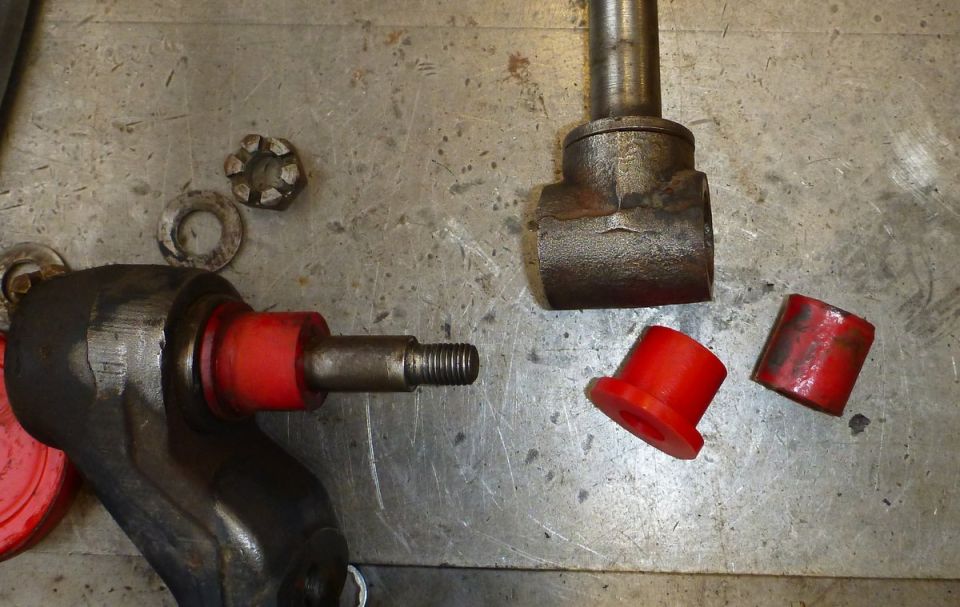 Black metal bracket with red bushing and threaded rod, red bushings, castle nut, and washers on metal surface.