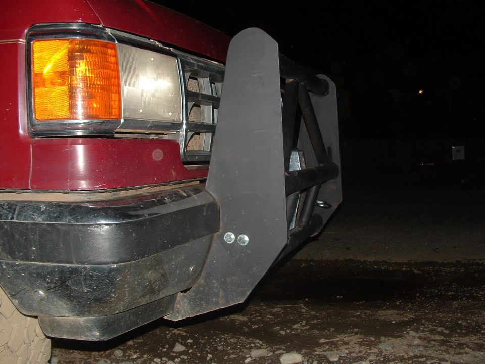 Night close-up of a maroon Ford front end showing headlight, amber marker and brush guard mount
