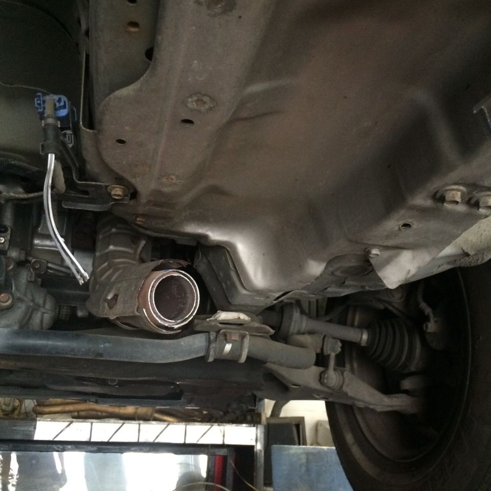 Underside of a car showing a damaged catalytic converter and exhaust pipe.