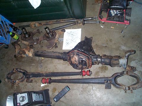 1981 Ford Bronco - Various Dana 44 axle components are spread across a concrete surface, including the differential housing and axle shafts.
