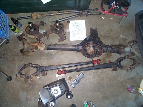 1981 Ford Bronco - Vehicle axle and suspension parts are laid out on the floor, possibly for repair or modification.