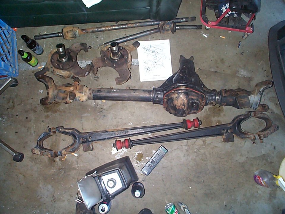 Front axle housing, radius arms with red bushings, knuckles and axle shafts on a garage floor
