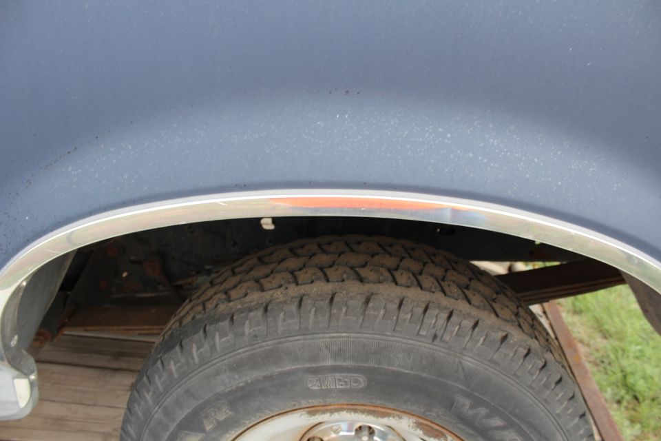 Dark blue vehicle rear wheel well with chrome trim and tire.