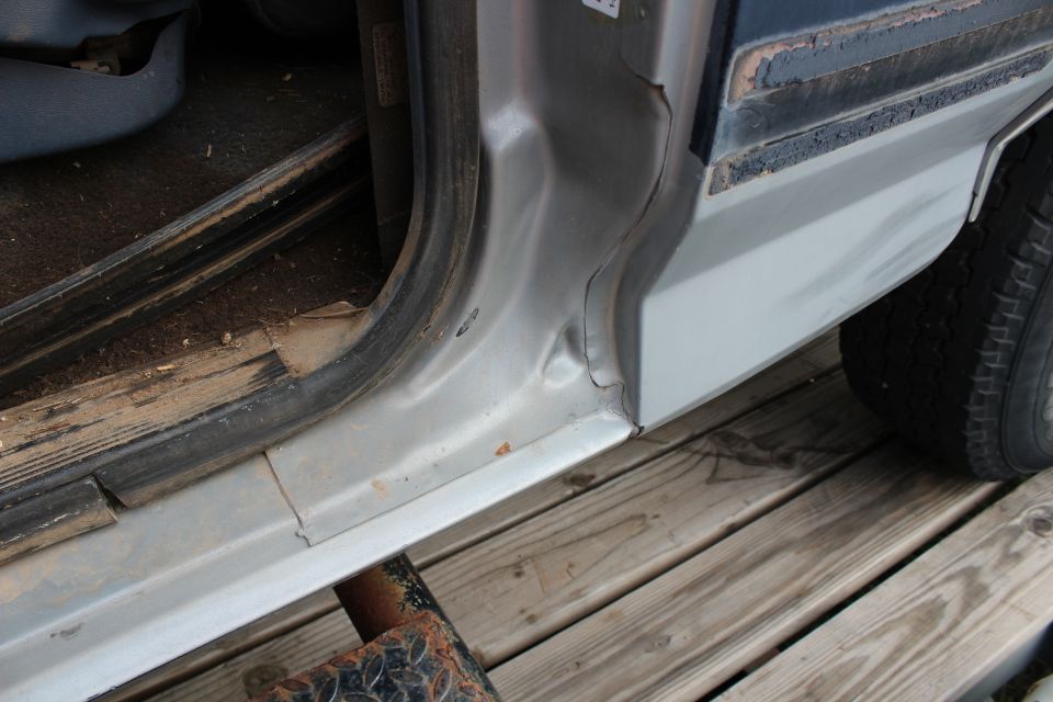 Damaged lower door frame and rocker panel of a vehicle, with rust and dents.