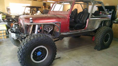 1985 Jeep CJ7 - A custom-built red Jeep CJ7 is shown in a garage setting, featuring a roll cage, racing seats, and large off-road tires. The front end is p…