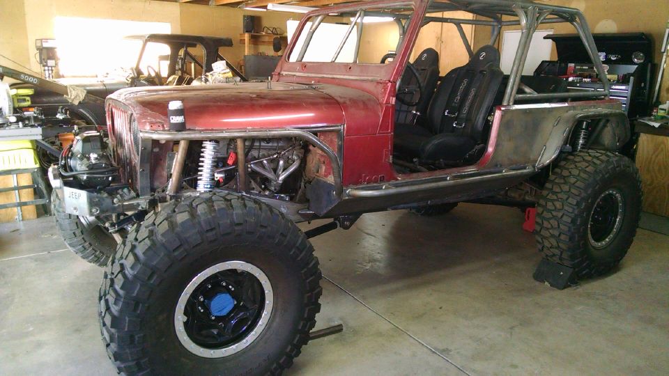 Custom red Jeep CJ7 with roll cage, racing seats, and large tires in a garage.