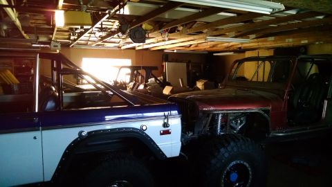 1985 Jeep CJ7 - Two off-road vehicles are parked side-by-side in a garage. The vehicle on the left is a blue and white SUV, while the vehicle on the right…