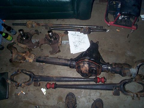 1981 Ford Bronco - Various Dana 44 axle components are laid out on a concrete surface, including a differential housing and drive shafts.