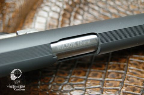 1979 Ford Bronco - A close-up shot of a firearm barrel with "WILSON 10mm" engraved on it. The firearm rests on a textured brown surface, possibly alligator sk…