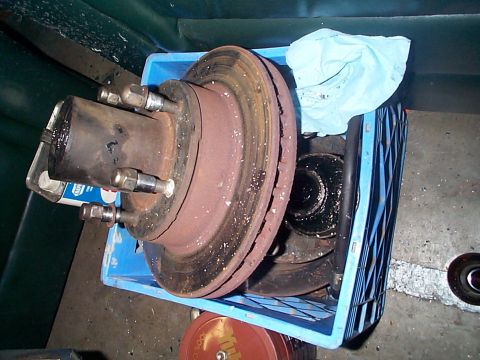 1981 Ford Bronco - Dana 44 axle parts, including a brake rotor and hub assembly, are stored in a blue plastic crate.