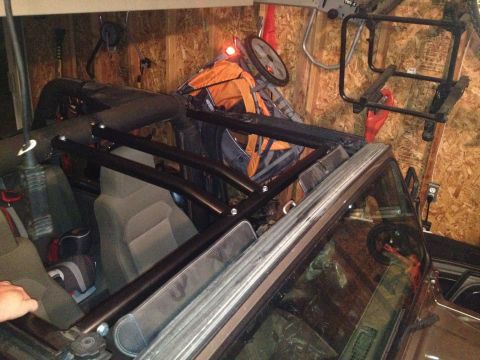 2005 Jeep Wrangler - A black roll cage is installed inside a Jeep Wrangler, which is parked in a garage with tools and equipment in the background.