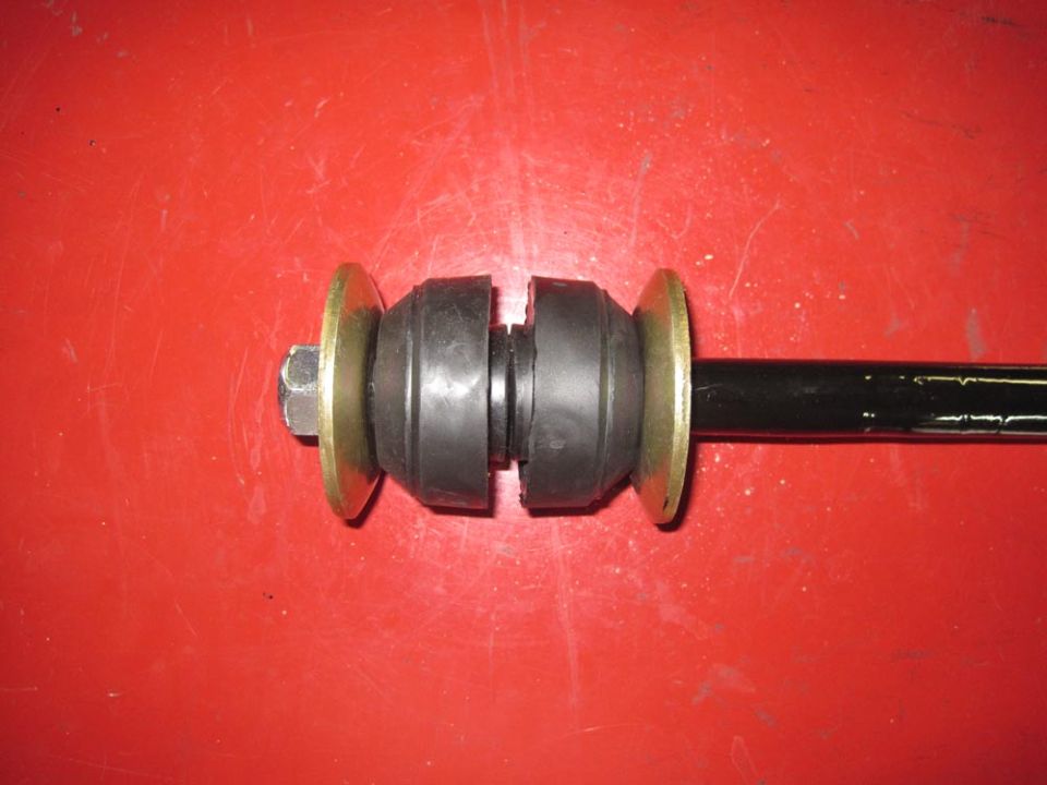Sway bar end link assembly with rubber bushings and brass washers, on red background. Supermotors.net logo in corner
