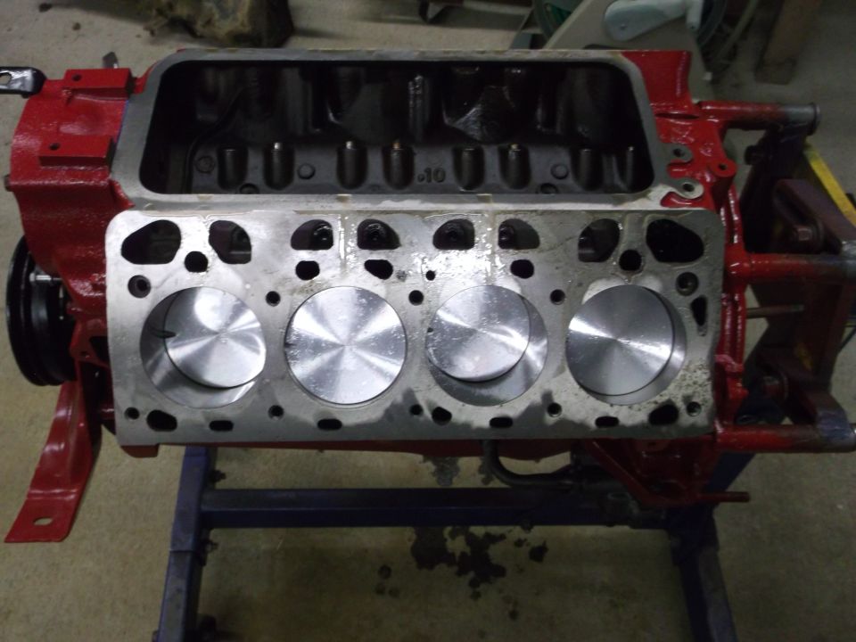 Red V8 engine block on a stand with head removed showing four new flat-top pistons in the bores