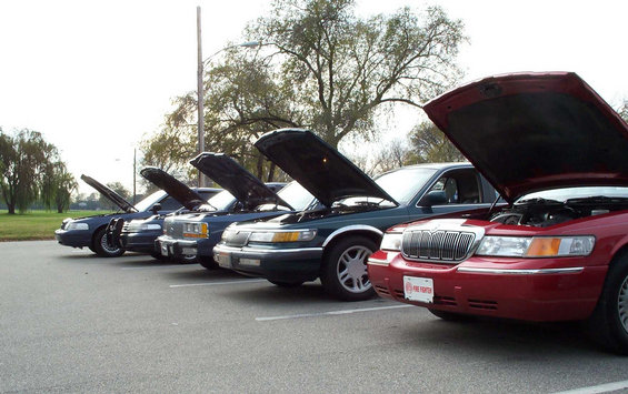 Five sedans with hoods open lined up in a parking lot, red Mercury Grand Marquis in front