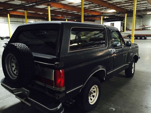 1988 Ford Bronco - A dark gray Ford Bronco is parked indoors, with a spare tire mounted on the back.