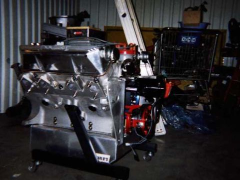 1963 Ford Fairlane - A polished V8 engine sits on a stand in a workshop, next to a shopping cart.